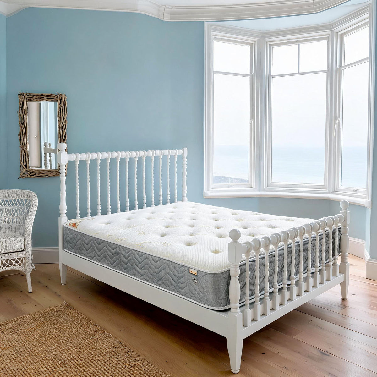 Carter & Lewis Memory Collection mattress with grey border on a white spindle bed in a seaside bedroom