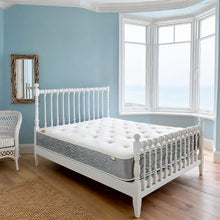 Carter & Lewis Memory Collection mattress with grey border on a white spindle bed in a seaside bedroom